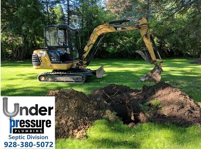 Excavator digging a trench in a grassy area for Under Pressure Plumbing septic services.