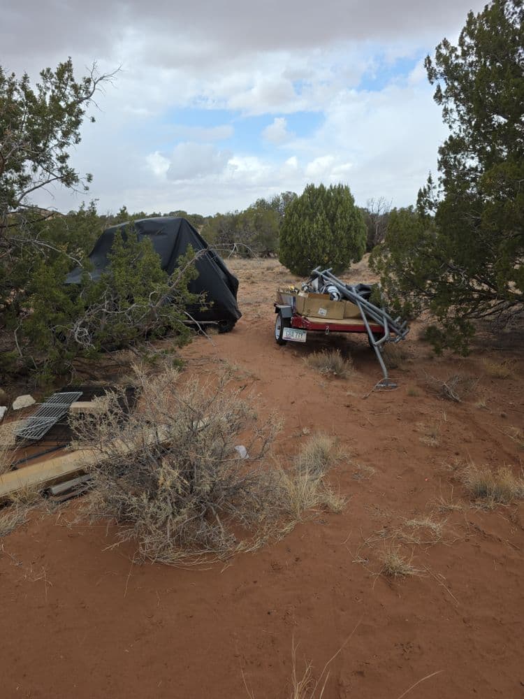 Camping setup in a desert landscape with a tent and trailer among shrubs and sand.