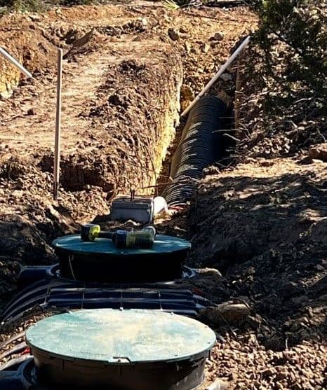 Underground drainage system installation with pipes and access covers in excavated trench.