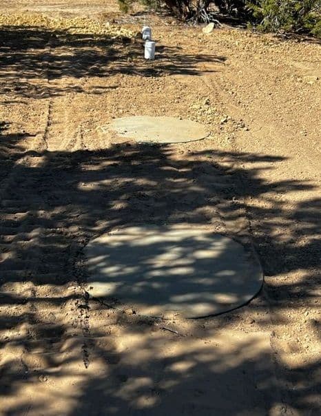 Concrete pads in a dirt area with a utility fixture, surrounded by sparse vegetation.