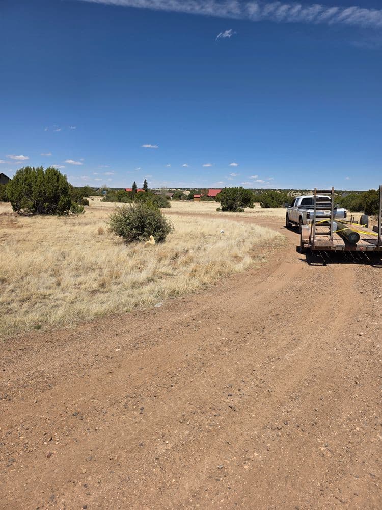 Dusty dirt road winding through open landscape with sparse vegetation and distant buildings.