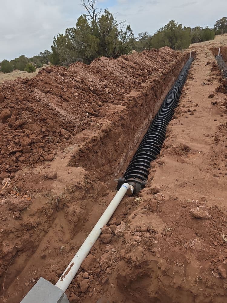 Underground piping in a trench surrounded by excavated soil and vegetation.