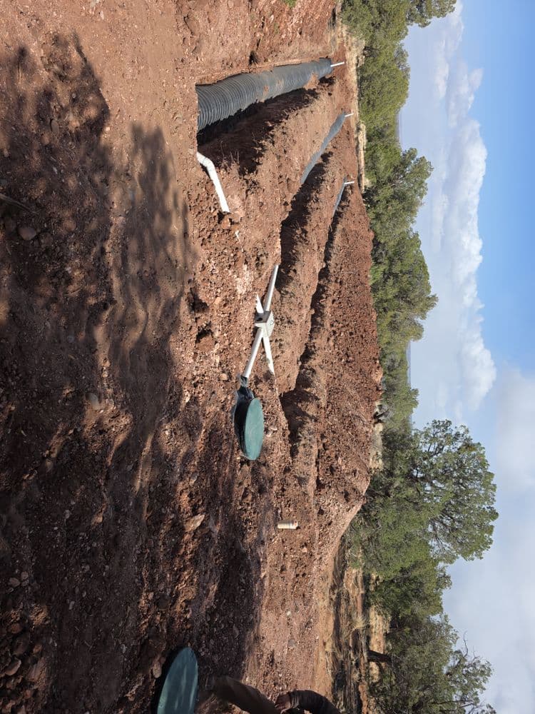 Excavated site with drainage pipes and mounds of earth under a clear blue sky.