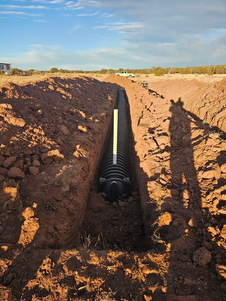 Excavated trench with drainage pipe installation in arid landscape under cloudy sky.