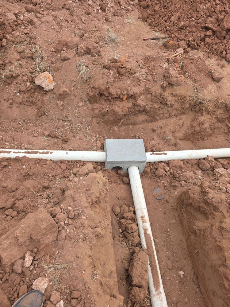 Underground utility junction box with white PVC pipes in a dug trench.