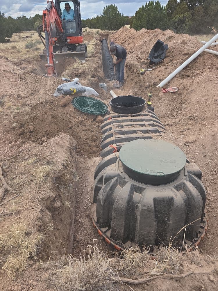 Excavation site for septic system installation with tanks and construction equipment.