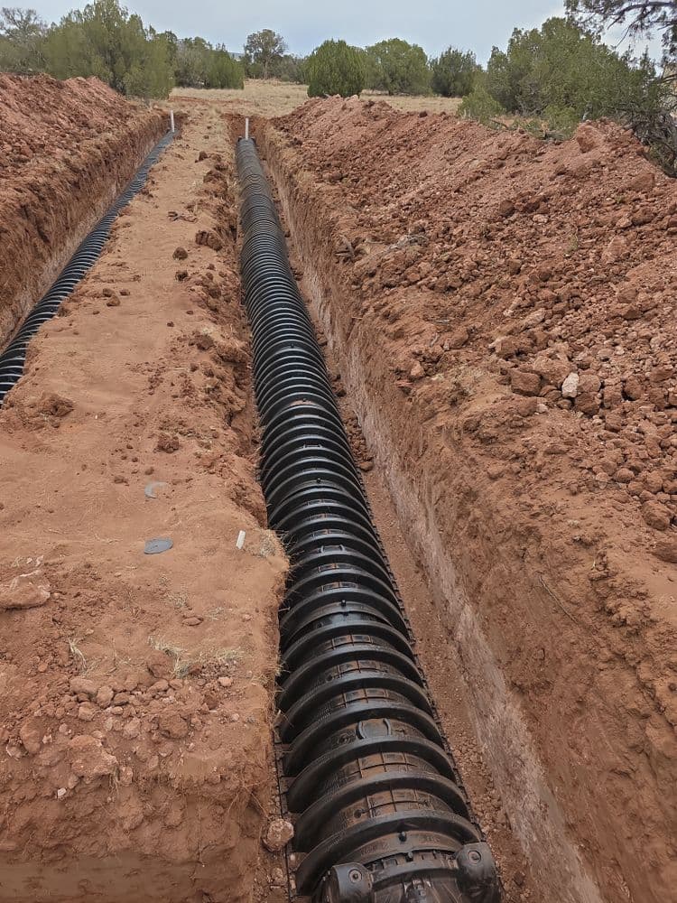 Underground drainage pipe installed in a freshly dug trench in dry, sandy soil.