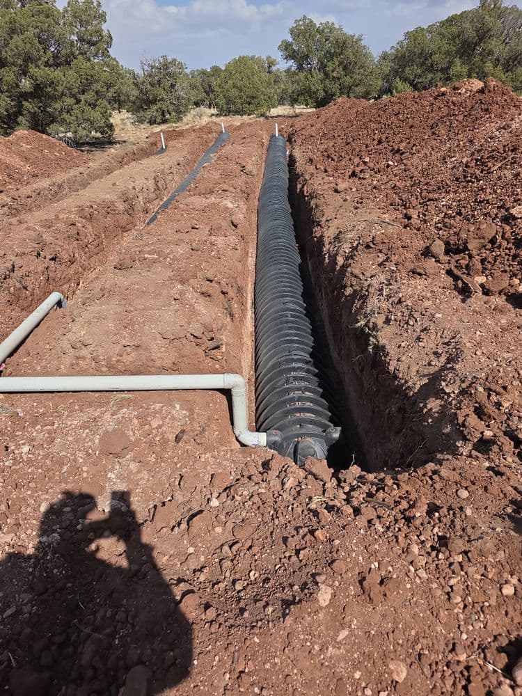 Excavated trench for drainage system installation in red soil landscape.