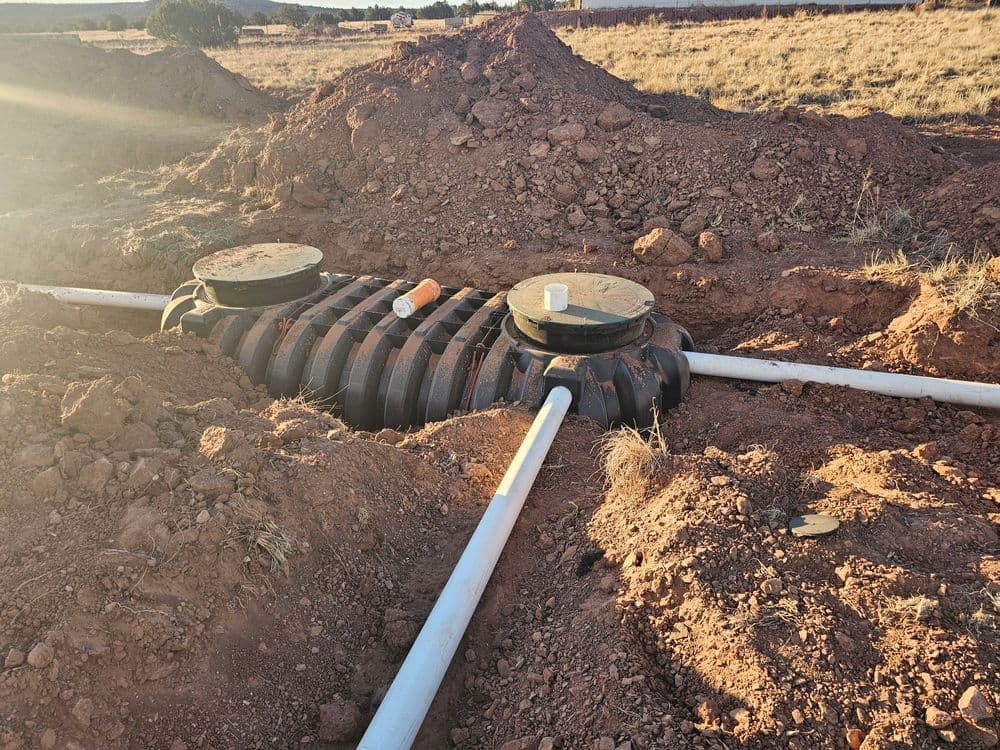 Septic tank installation in a trench with pipes surrounded by dirt and sunlight.