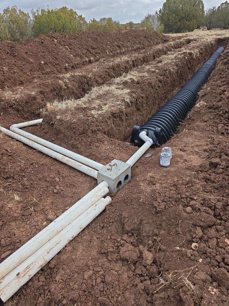 Underground drainage system installation with black pipe and PVC components in a trench.