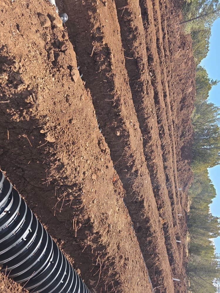 Excavated soil with horizontal trenches and black drainage pipes in a rural landscape.