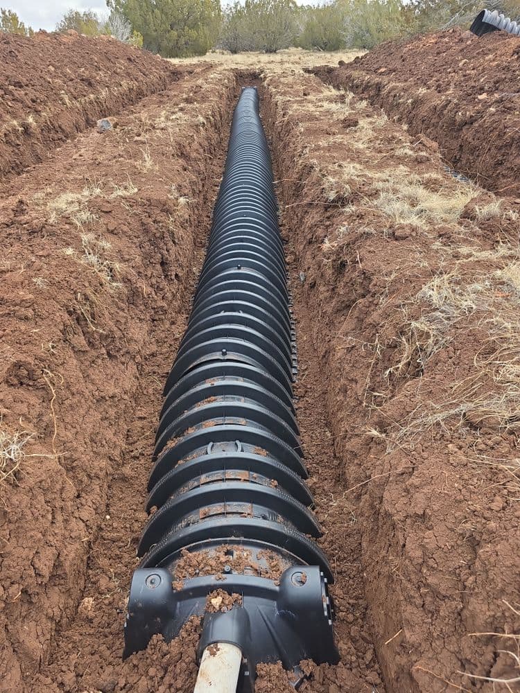 Corrugated drainage pipe installed in a deep, freshly dug trench in dry soil.