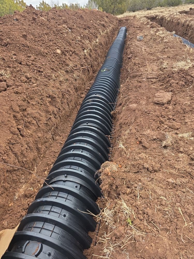 Black drainage pipe installed in a freshly excavated trench on a construction site.
