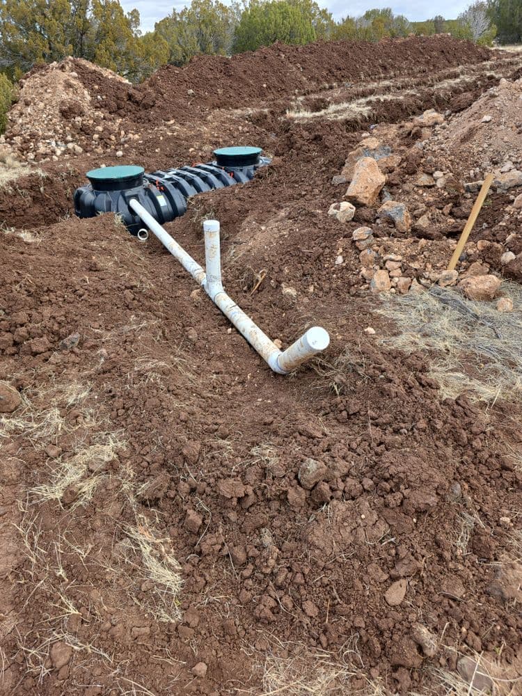 Installation of a sewer system with PVC pipes and tanks in a trench on a construction site.